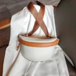 sac banane femme chic en cuir blanc cassé et marron posé sur une chaise