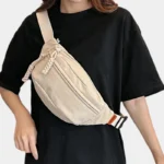 sac banane beige porté en banoulière par une femme habillée en noir