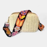 Bandoulière Brodée Bohème Motifs Floraux noire à fleurs multicolores avec mousquetons métallisés dorés, posée sur un sac clair.