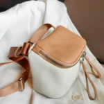 Sac à Main Banane Cuir Femme en cuir blanc et brun avec une lanière et une fermeture éclair visible sur un fond de tissu