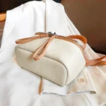 Sac à Main Banane Cuir Femme de couleur blanche en cuir avec une lanière beige posé sur une surface claire