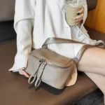 Sac à Main Banane Cuir Femme gris mat posé sur un banc avec une bandoulière et double zip