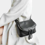 Sac à Main Banane Cuir Femme en cuir noir porté sur le côté avec une texture grainée