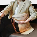 Sac Banane Femme Cuir Chaîne Dorée beige porté élégamment sur l'épaule Sac Banane Femme Cuir Chaîne Dorée de couleur beige porté sur l'épaule par une femme en blazer