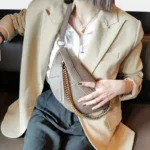 Sac Banane Femme Cuir Chaîne Dorée gris élégant porté en travers du corps Sac Banane Femme Cuir Chaîne Dorée gris porté en travers du corps par une femme avec un blazer clair