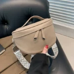 Sac Banane Femme Cuir Chic Bandoulière de couleur beige avec une sangle aux motif géométrique dans une main