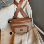 Sac Banane Femme Cuir Chic Bicolore Sac Banane Femme Cuir Chic Bicolore en cuir beige et marron avec une poche avant zippée posé sur un manteau