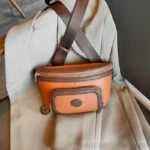 Sac Banane Femme Cuir Chic Bicolore marron orange élégant posé sur un manteau Sac Banane Femme Cuir Chic Bicolore marron et orange posé sur un manteau beige avec une lanière en nylon