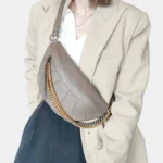 Sac Banane Femme Cuir Chaîne Dorée en cuir gris avec chaîne dorée porté en bandoulière Sac Banane Femme Cuir Chaîne Dorée gris avec une chaîne dorée porté en bandoulière sur un haut clair