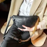 Sac Banane Femme Cuir Chaîne Dorée cuir noir et chaîne dorée élégant Sac Banane Femme Cuir Chaîne Dorée noir avec chaîne dorée porté sous le bras par une personne