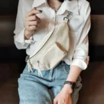 Sac Banane Femme Cuir Rock Chic blanc porté en travers du corps avec chemisier Sac Banane Femme Cuir Rock Chic de couleur blanche porté en travers du corps par une femme avec un chemisier blanc