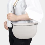 Sac Banane Femme Moderne Cuir blanc cassé beige porté en bandoulière avec sangle Sac Banane Femme Moderne Cuir de couleur blanc cassé beige porté en bandoulière avec une sangle sur un vêtement blanc