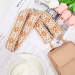 Bandoulière Motifs Jacquard Nordique beige avec motifs floraux et mousquetons dorés attachée à un sac clair.