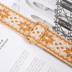 Bandoulière Motifs Jacquard Nordique orangée avec boucle de réglage en métal doré sur fond de magazine.