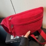 Banane en velours côtelé rouge posée de face, avec fermeture zippée ornée de liens tressés