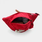 Banane en velours côtelé rouge vue de dessus, poche principale ouverte révélant divers essentiels à l'intérieur