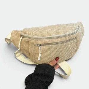 Sac banane velours côtelé beige sablle posé de face, tenu par une main avec deux fermetures éclair apparentes
