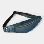 Petit sac banane cuir bleu à fermeture dorée posé à plat, vu de dessus avec sangle noire