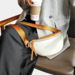 Sac banane cuir grainé blanc porté en bandoulière par une femme, avec large sangle contrastante