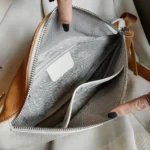 Sac banane cuir grainé blanc et camel posé vu de dessus, poche principale ouverte doublure chevron et poches zippées