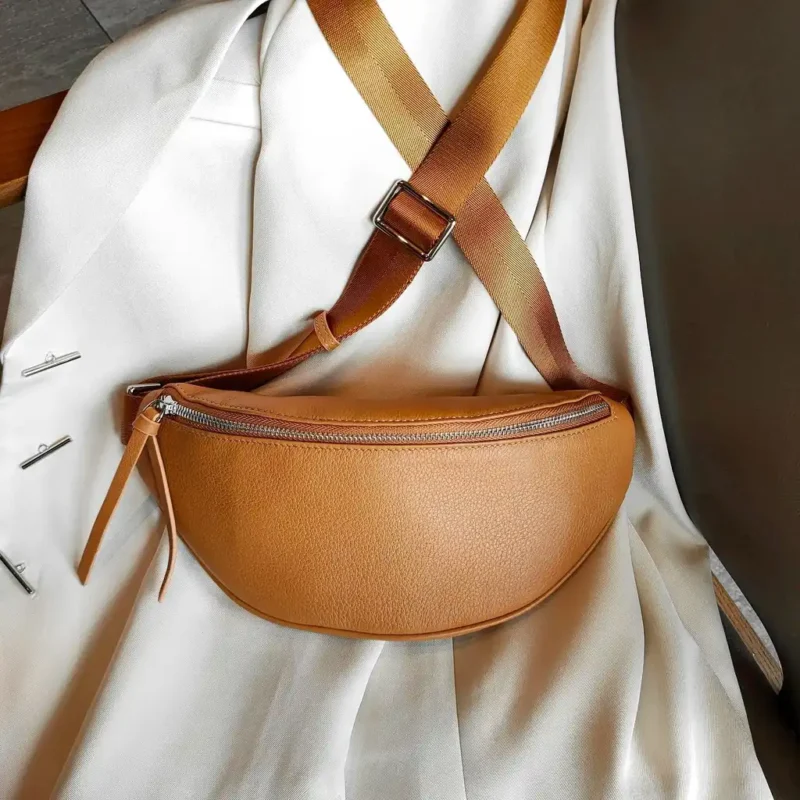 Sac banane cuir grainé camel posé de face sur une veste, avec sangle bicolore et fermeture métallique chromée