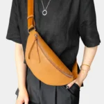 Sac banane cuir grainé camel porté en bandoulière par une femme, fermeture zippée avec languette