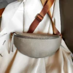 Sac banane cuir grainé femme gris posé de face, avec large sangle bicolore et fermeture chromée