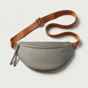 Sac banane cuir grainé femme demi-lune gris clair posé à plat, avec sangle marron et fermeture zippée métal chromé