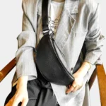 Sac banane cuir grainé noir porté en bandoulière par une femme au style chic vue rapprochée