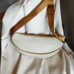 Sac banane cuir grainé beige posé à plat vu de dessus avec sangle bicolore marron et attache métal