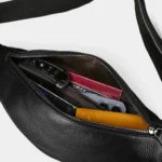 Petit sac banane cuir noir grainé, vu de dessus avec poche principale ouverte contenant clés et portefeuille