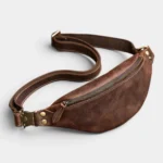 Petit sac banane en cuir marron vintage posé à plat vue de face avec fermeture éclair bronze et attache en métal