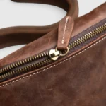 Petit sac banane cuir marron vu de près, avec fermeture éclair métallique et surpiqûres contrastantes
