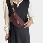 Sac banane bordeaux porté en bandoulière par une femme, au style chic, avec sangle à motif chevron beige