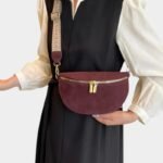 Sac banane simili cuir bordeaux porté en bandoulière par une femme avec sangle à motif tressé et zip doré