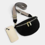 Sac banane noir en simili cuir posé de face vu de dessus avec sangle à motifs beiges et fermeture zippée dorée