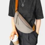 Sac banane cuir grainé gris porté en bandoulière par une femme, avec une sangle large contrastante