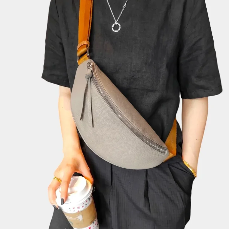 Sac banane cuir grainé gris porté en bandoulière par une femme, avec une sangle large contrastante