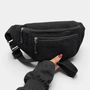 Sac banane velours côtelé noir profond posé de face, tenu par une main avec deux fermetures éclair apparentes