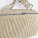 Sac banane velours côtelé beige posé de face, avec sangle motif chevron et fermeture zippée métallique