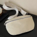 Sac banane velours côtelé beige posé à plat de face, avec sangle à motif chevron clair et fermeture zippée chromée