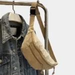 Sac banane velours côtelé beige posé de face sur un portant, avec sangle unie et deux fermetures à zip métal