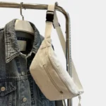 Sac banane velours côtelé beige posé en bandoulière de face, avec sangle épaisse à clip plastique noir