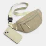 Sac banane velours côtelé beige posé à plat de face, avec sangle claire et clip plastique noir à côté d’un smartphone