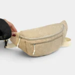 Sac banane velours côtelé beige posé de face sur fond clair, une main féminine tient l'extrémité