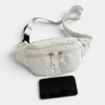 Sac banane velours côtelé blanc posé à plat de face, avec fermeture zippée blanche et un smartphone placé devant