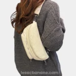 Sac banane velours côtelé écru porté en bandoulière par une femme de profil au style casual, avec sangle motif chevron