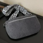 Sac banane velours côtelé gris posé de face, avec sangle à motif chevron noir et blanc