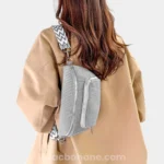 Sac banane velours côtelé gris clair porté sur l'épaule par une femme au style casual, avec sangle motif chevron