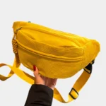 Sac banane velours côtelé jaune posé de face tenu à la main, avec sangle unie jaune à boucle plastique noire